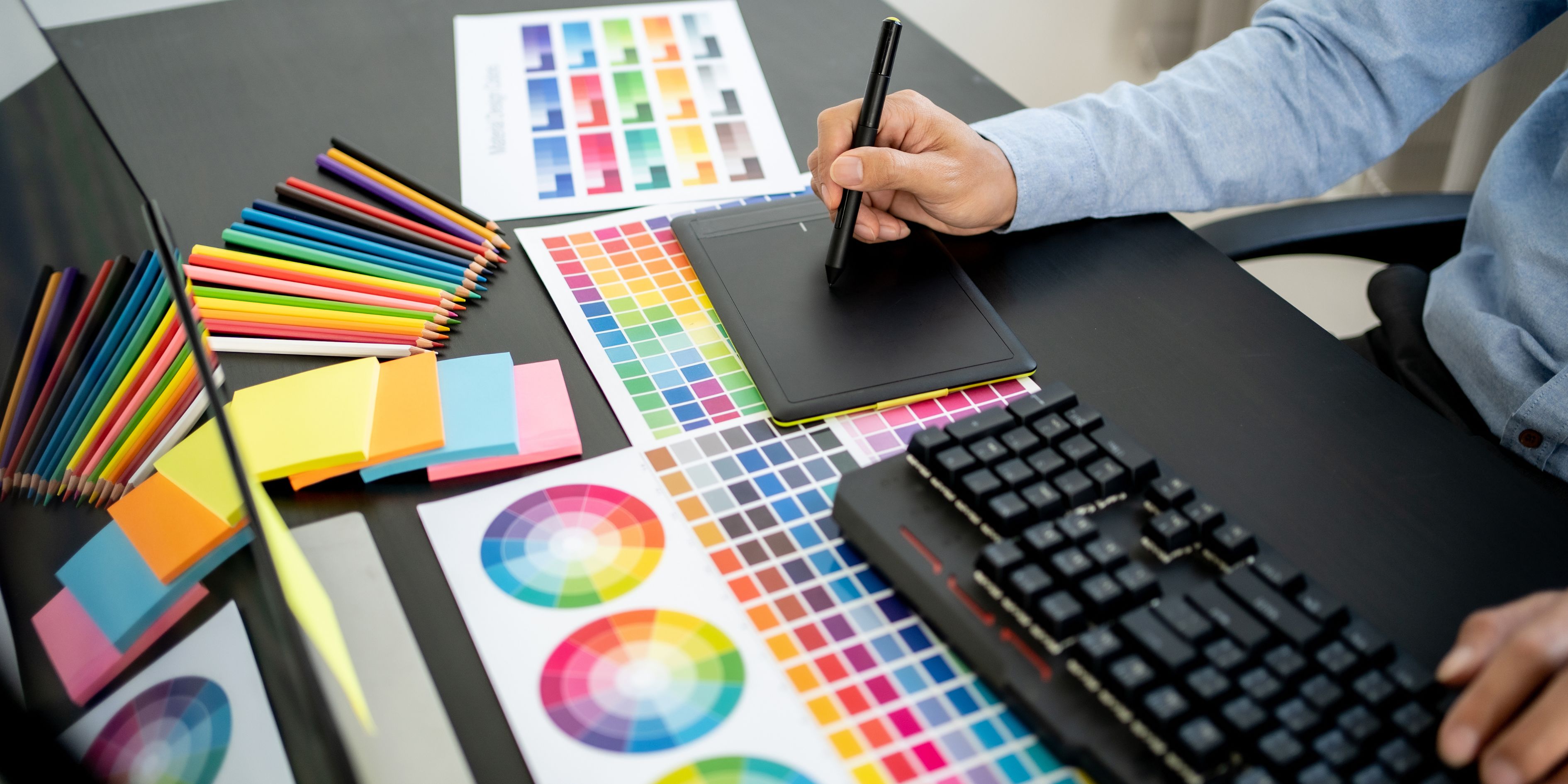 a hand of a person designing things with papers on the table and a keyboard on the side(design tools for solopreneurs)